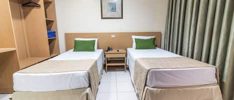 A hotel room with two beds, a wooden wardrobe, a small bedside table, and a framed picture on the wall.