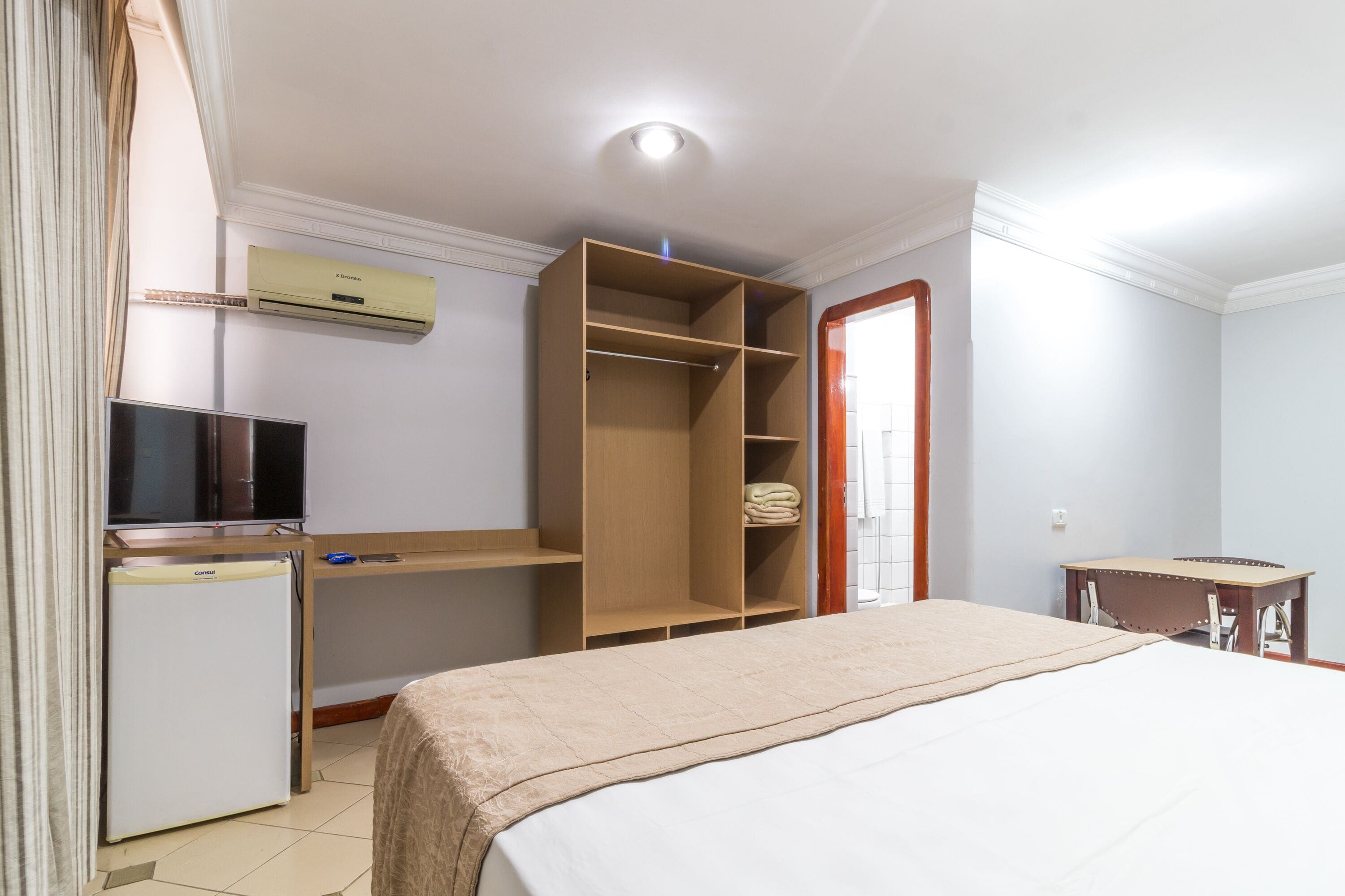 A hotel room with a bed, a wardrobe, a desk, a television, and a refrigerator.