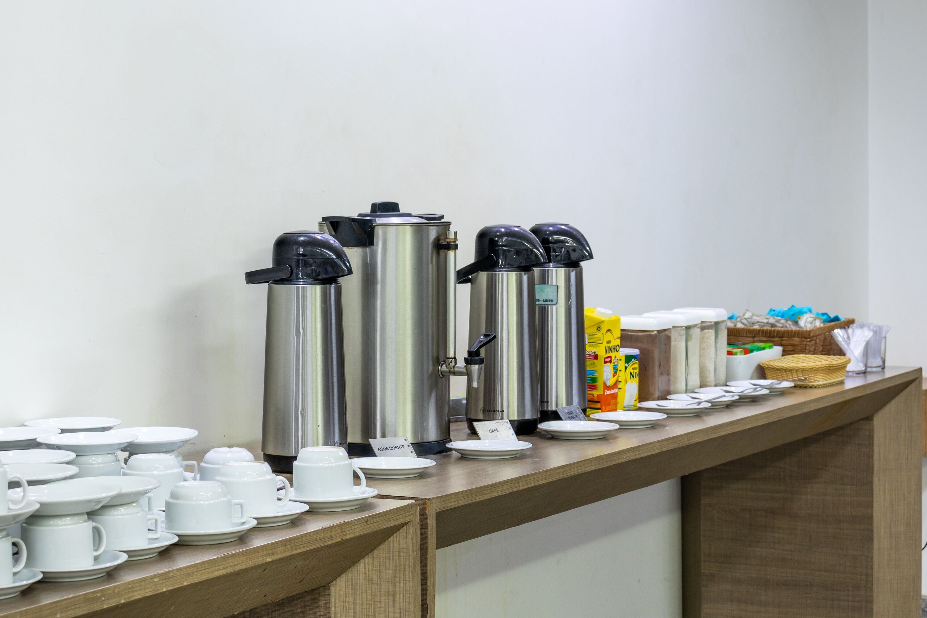 A buffet setup with various coffee machines, plates, and cups arranged on a counter.