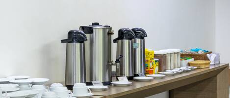 A buffet setup with various coffee machines, plates, and cups arranged on a counter.