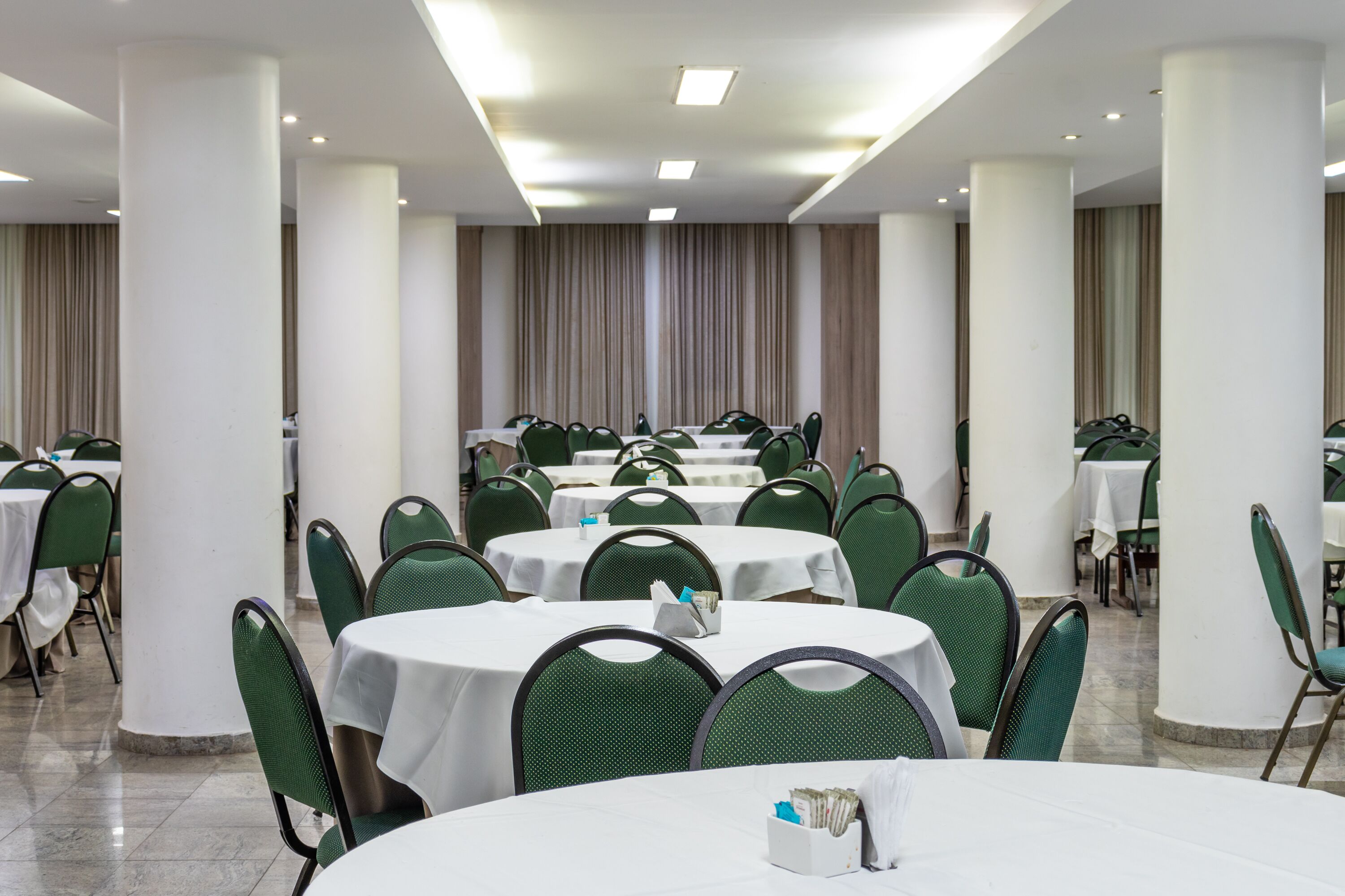 A conference room with round tables and green chairs, white tablecloths, and a neutral color scheme.