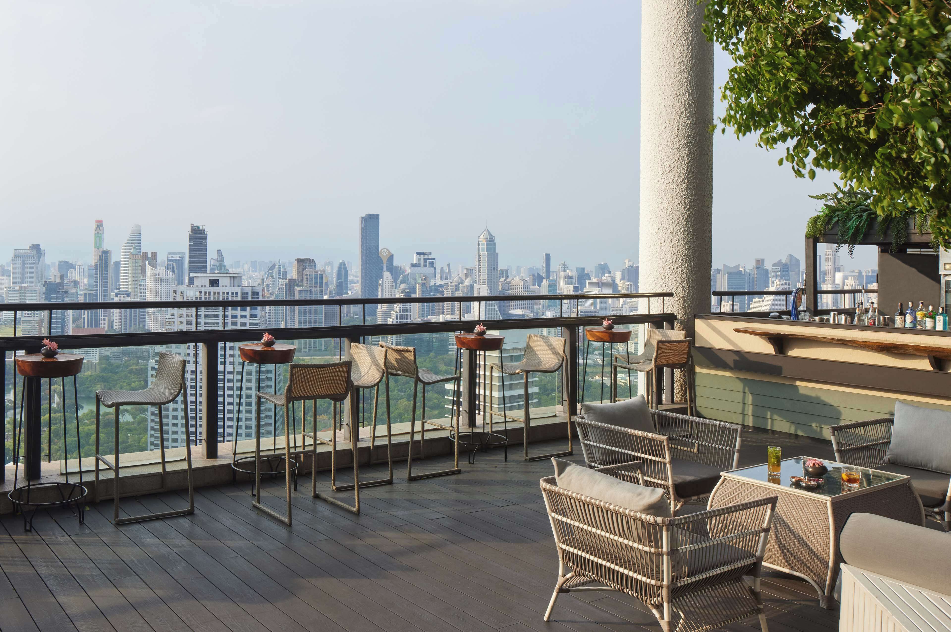 A rooftop terrace with wicker furniture, a glass table, and a view of a city skyline.