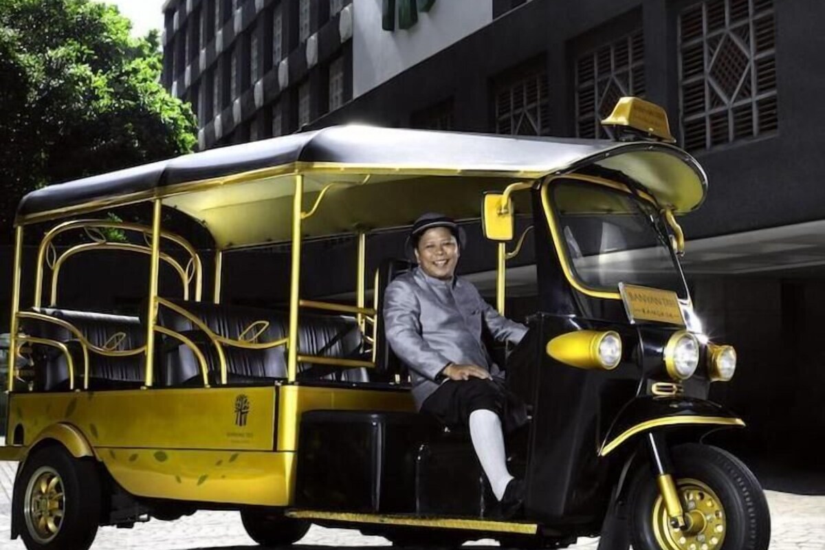 A yellow and black vintage-style vehicle parked in front of a building with a large green sign.