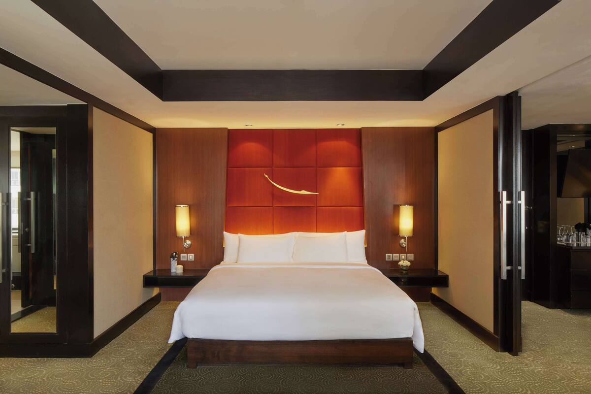 A hotel room with a large bed, wooden headboard, two bedside tables with lamps, and a mirror.