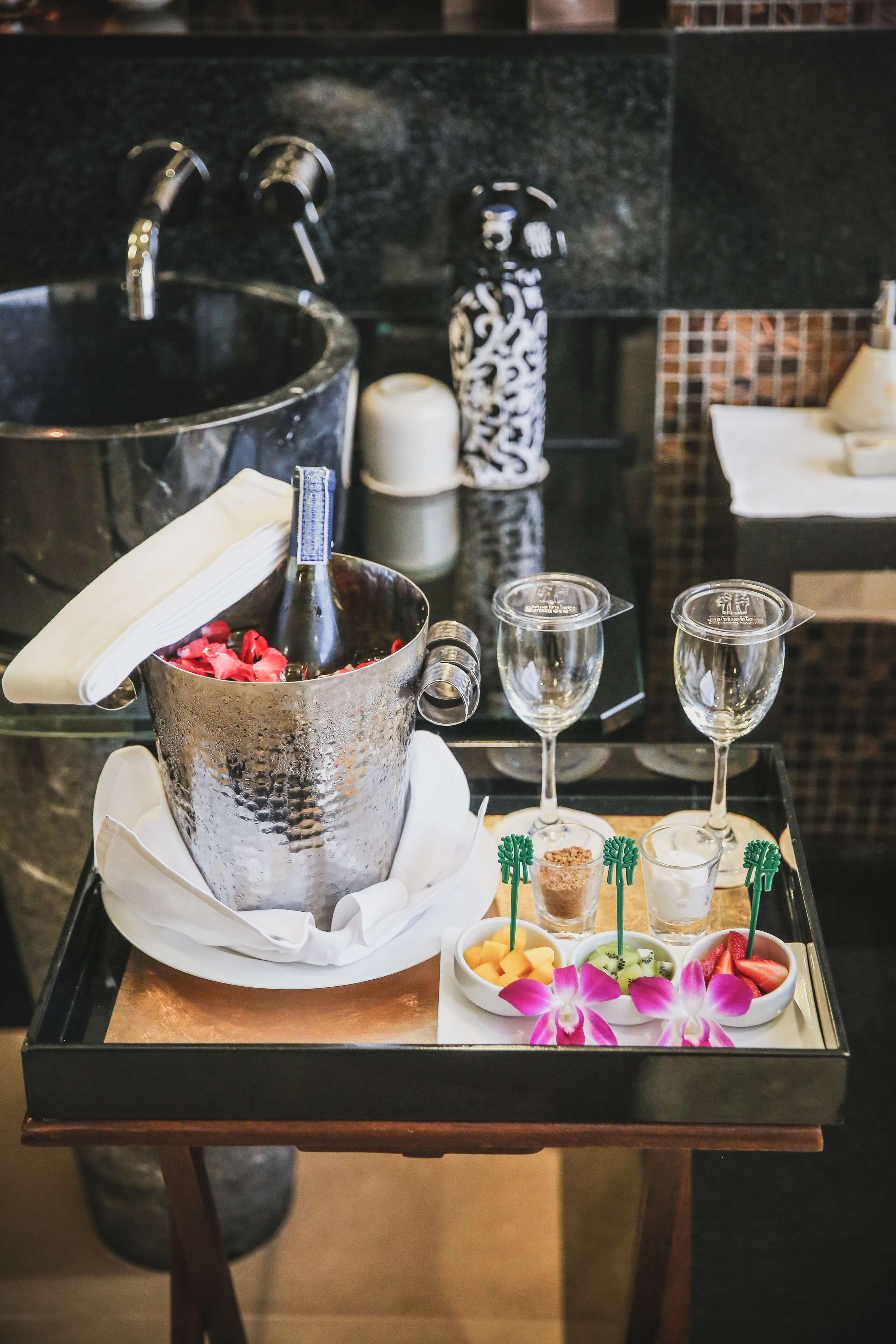 A tray with a bottle of champagne, two glasses, and a plate of fruit.