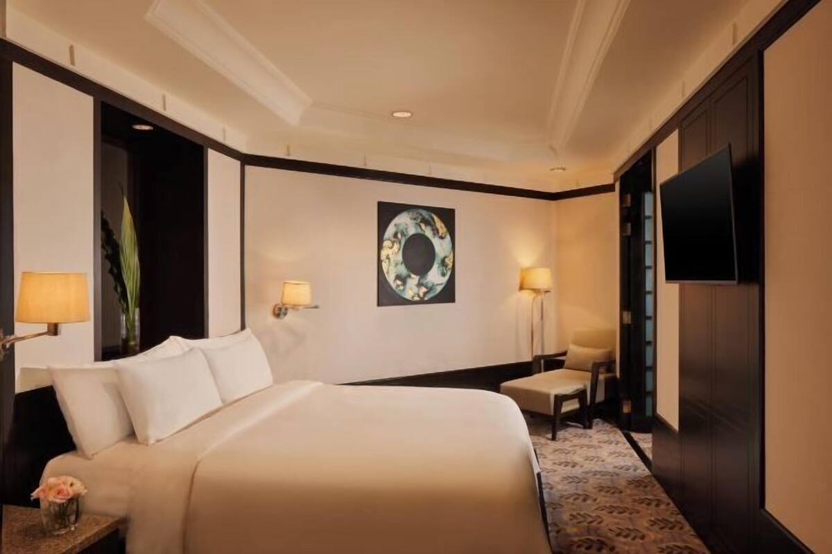 A hotel room with a large bed, bedside lamps, a wall-mounted TV, and a decorative wall piece.