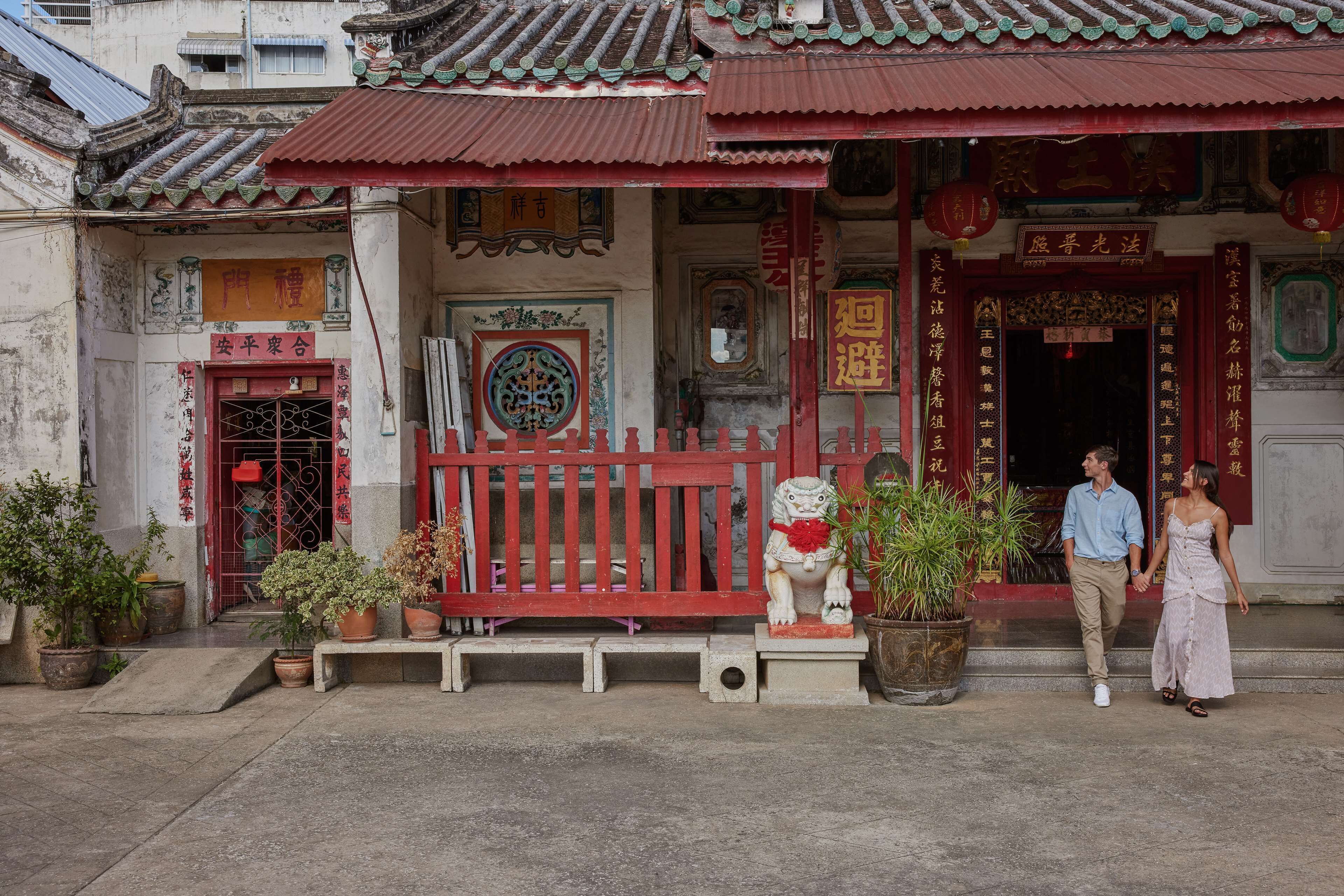 A traditional building with a red entrance, potted plants, and a lion statue.