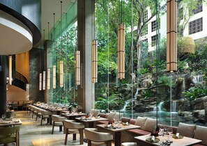A restaurant with a long dining table, multiple chairs, and hanging pendant lights.