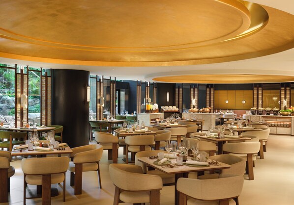 A spacious restaurant with multiple dining tables and chairs, a central column, and a view of the outdoors through large windows.
