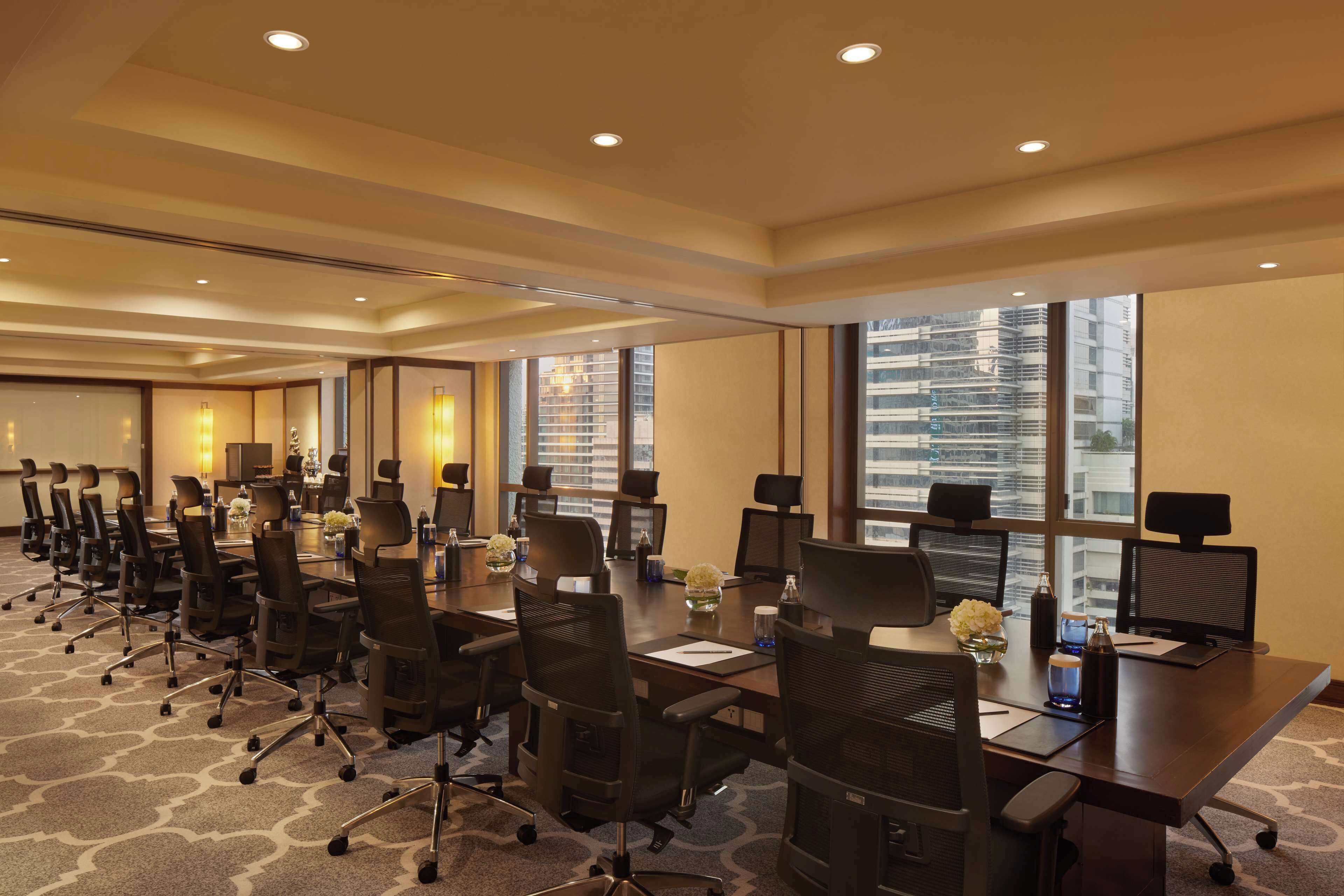 Un salón de conferencias con varias mesas, sillas y ventanas amplias que ofrecen vistas a la ciudad.