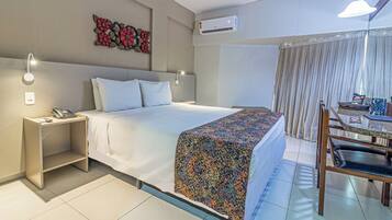 Habitació d'hotel amb un llit, una taula de nit amb un telèfon, un escriptori amb una cadira, un element decoratiu a la paret i un aparell d'aire condicionat.