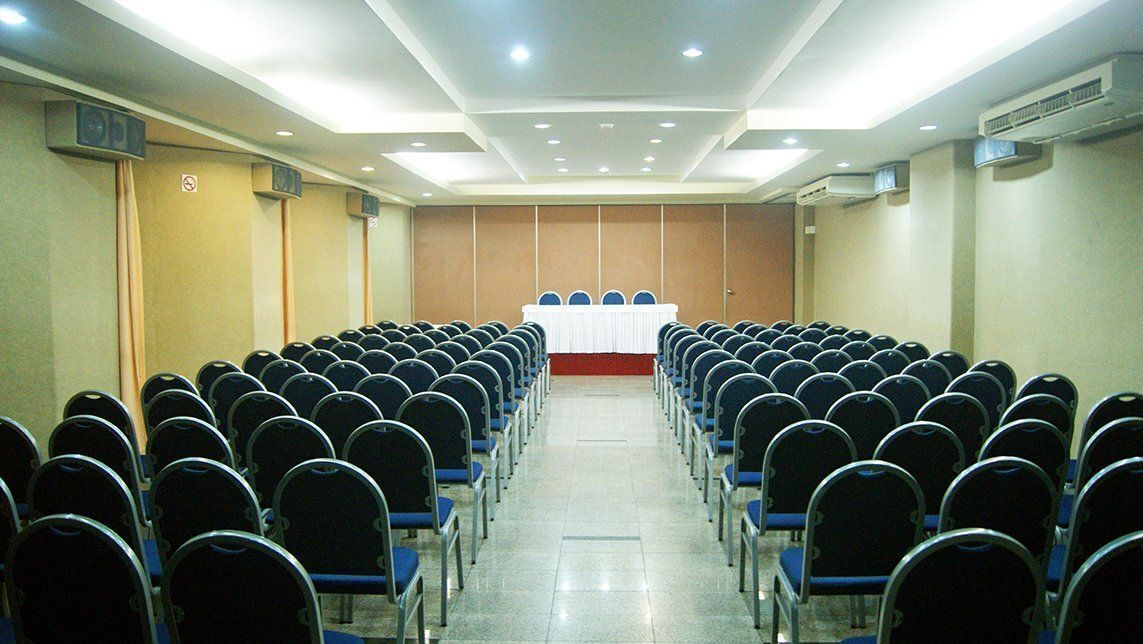 A conference room with rows of chairs facing a table with a red tablecloth.
