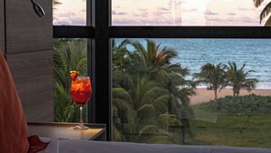 A room with a view of the ocean, a glass of red drink with a strawberry garnish, and a wooden table. - Littoral Hotel (João Pessoa)