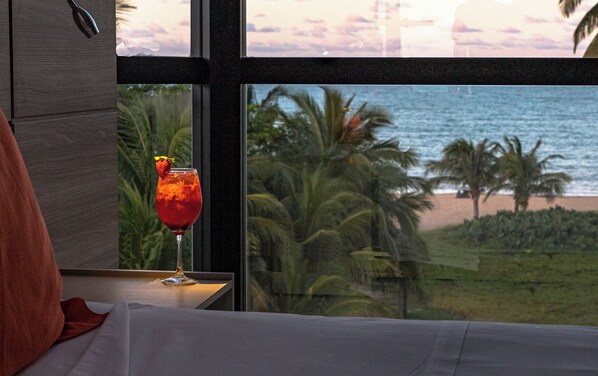 Una habitación con vista al océano, una copa de bebida roja adornada con una fresa y una mesa de madera.