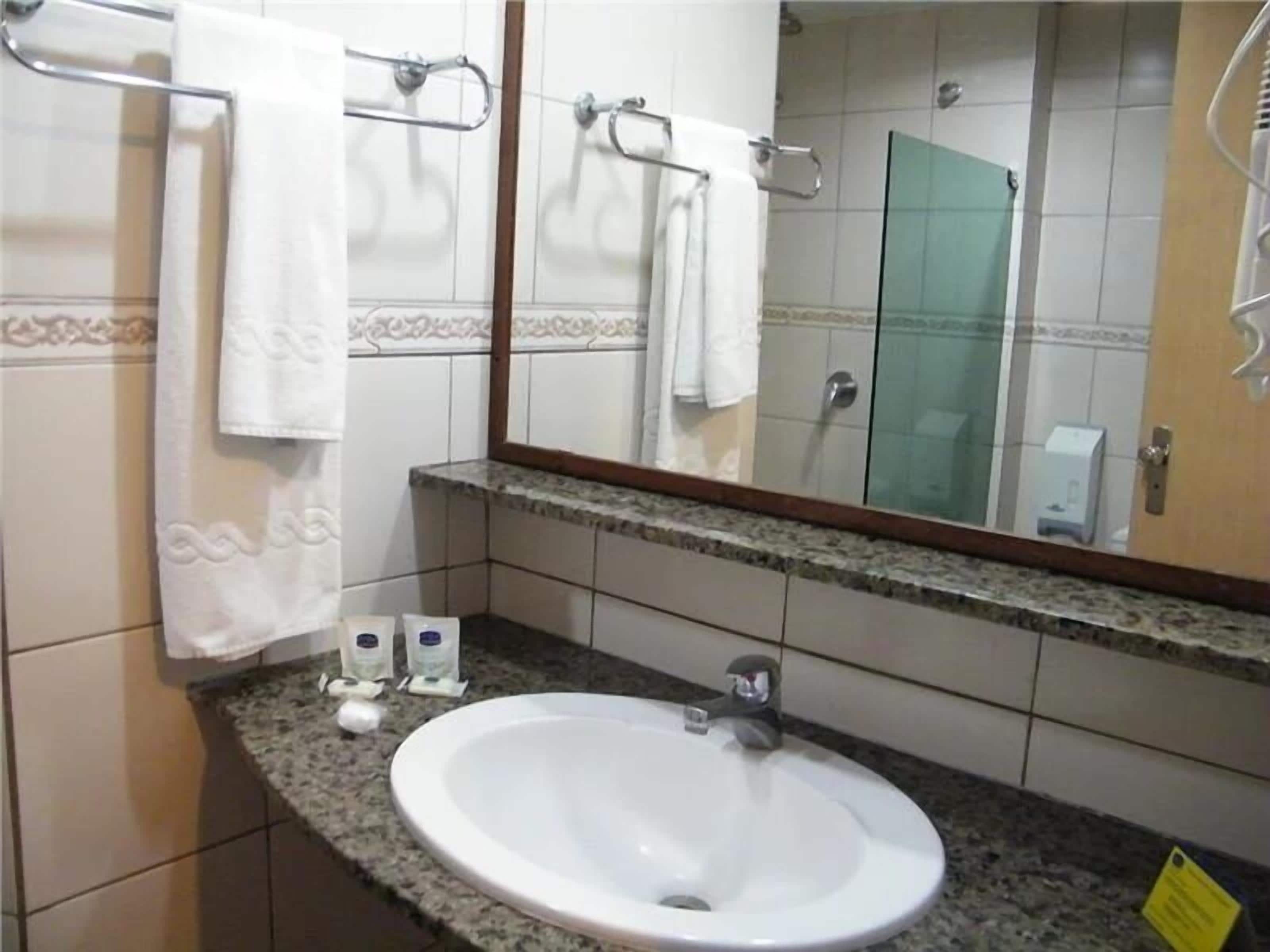 A bathroom with a sink, mirror, towel rack, and a glass shower enclosure.