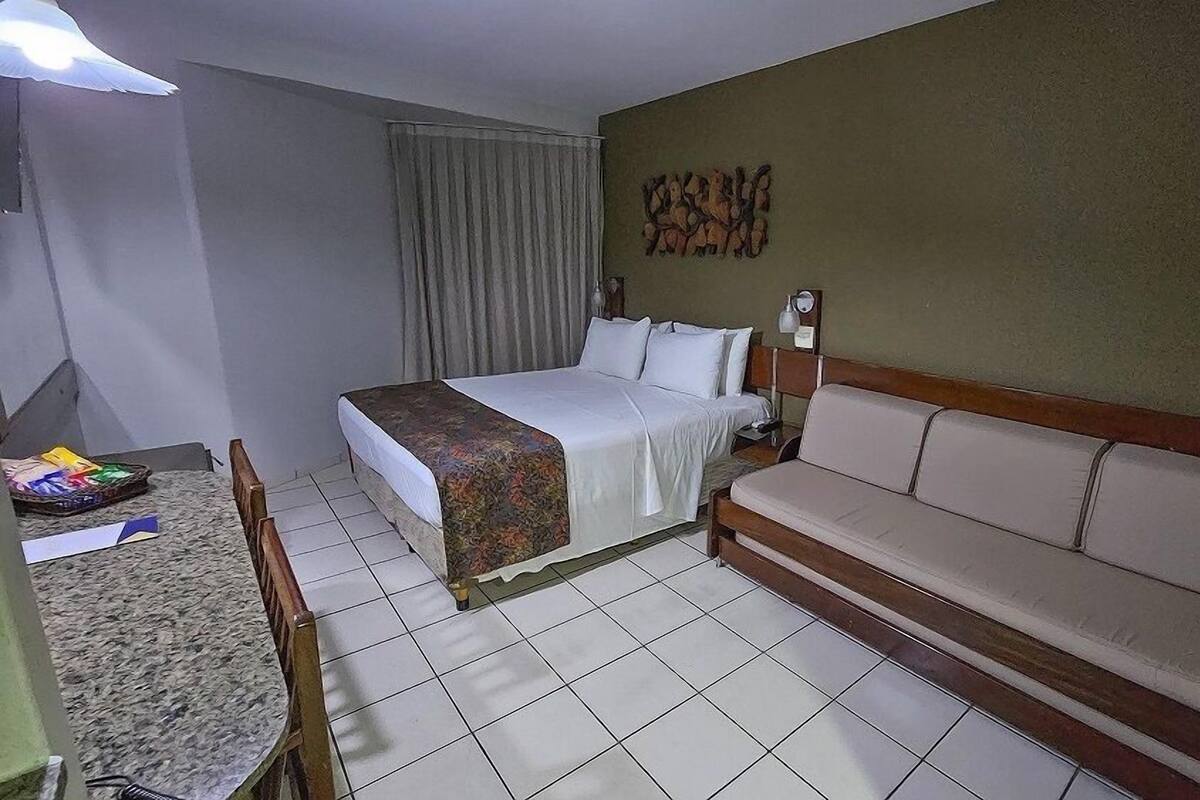 A hotel room with a bed, a sofa, a desk with a chair, a lamp, and a wall decoration.