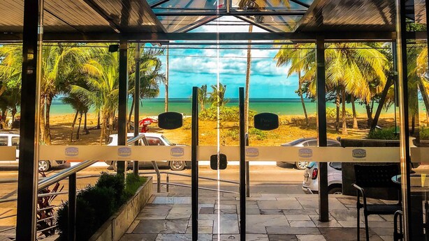 A covered outdoor seating area with a view of the beach and palm trees. - Littoral Hotel (João Pessoa)