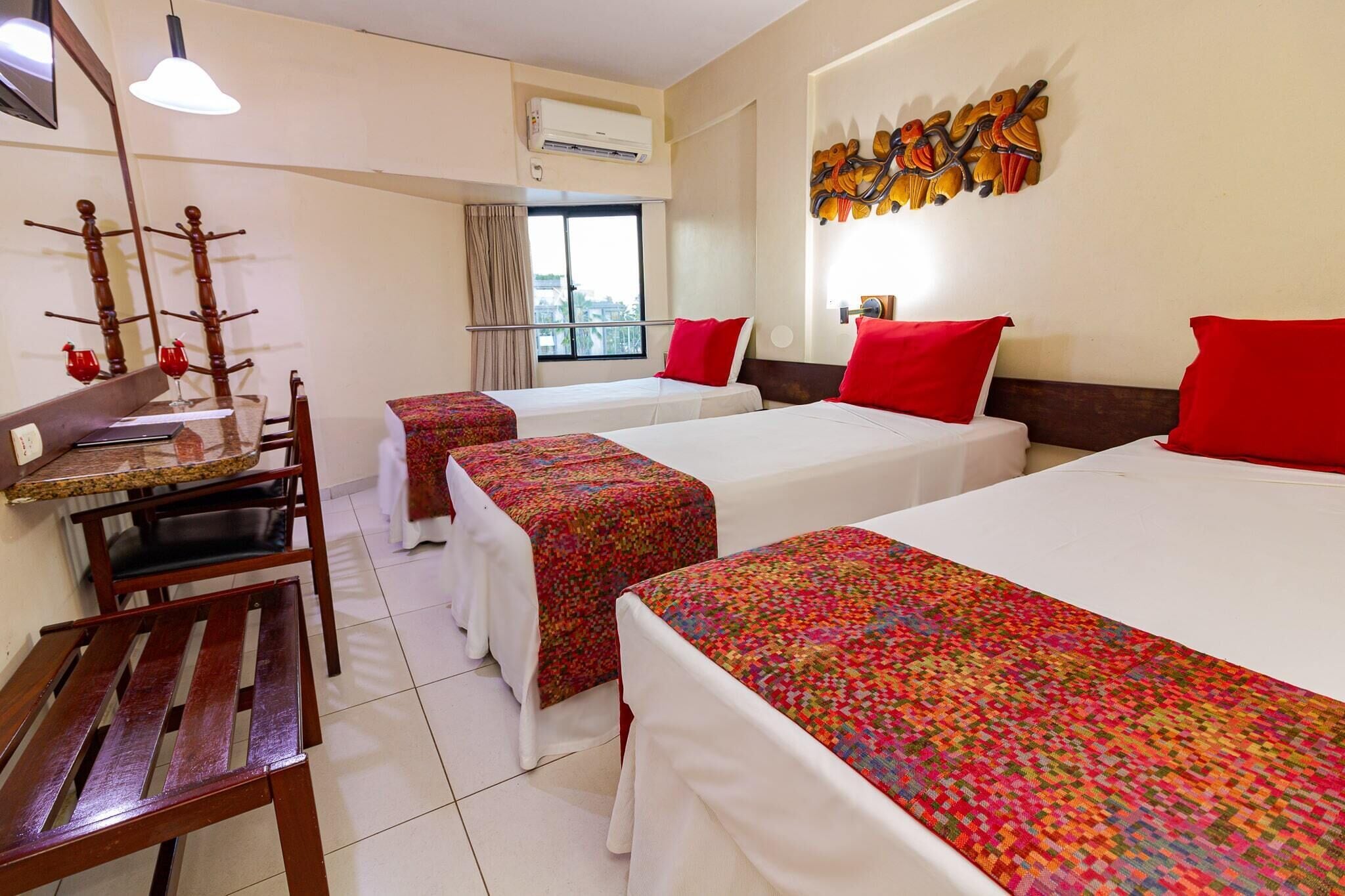 A hotel room with two beds, a desk, and a chair. There is a window with a view of the city.