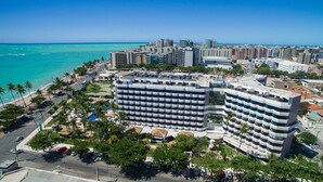 A high-rise hotel with multiple balconies, a beach view, and a parking area with cars. - Maceio Atlantic Suites (Maceió)