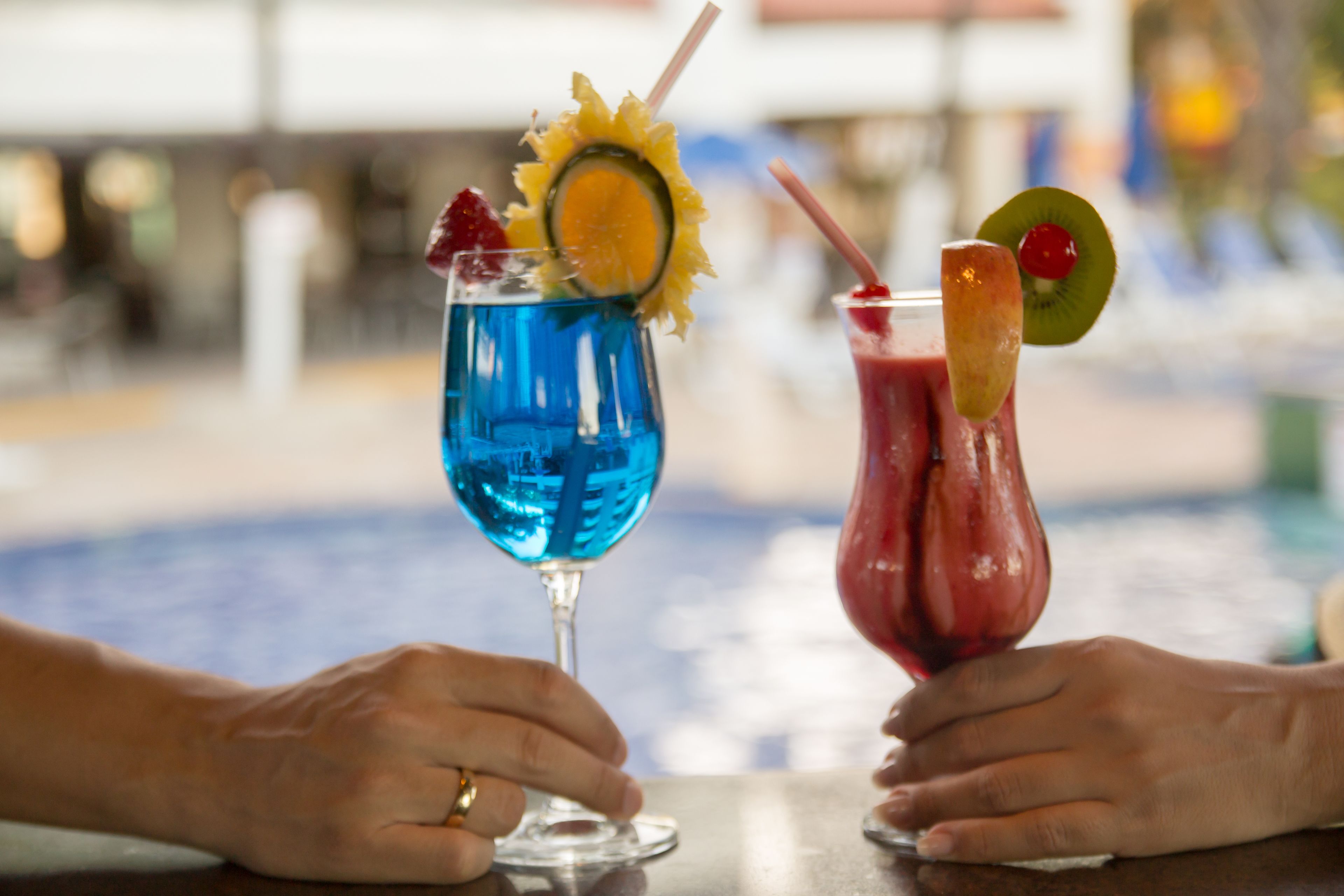 Two hands holding cocktail glasses with fruit garnishes.