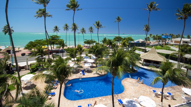 A resort with a swimming pool, palm trees, and a view of the ocean. - Maceio Atlantic Suites (Maceió)