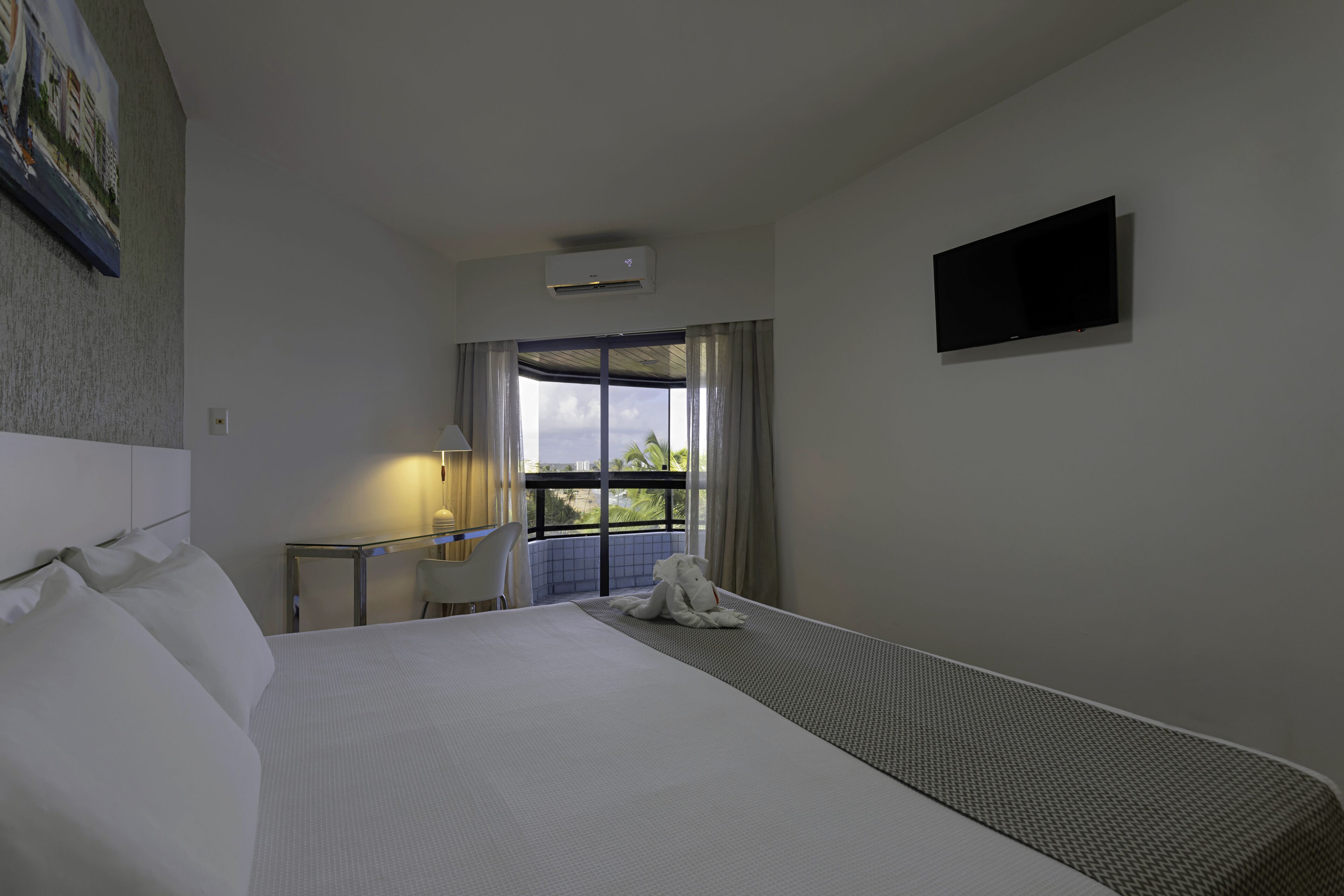 Una camera d'albergo con un letto grande, una scrivania con una sedia, una televisione a schermo piatto montata a parete e una finestra con tende.