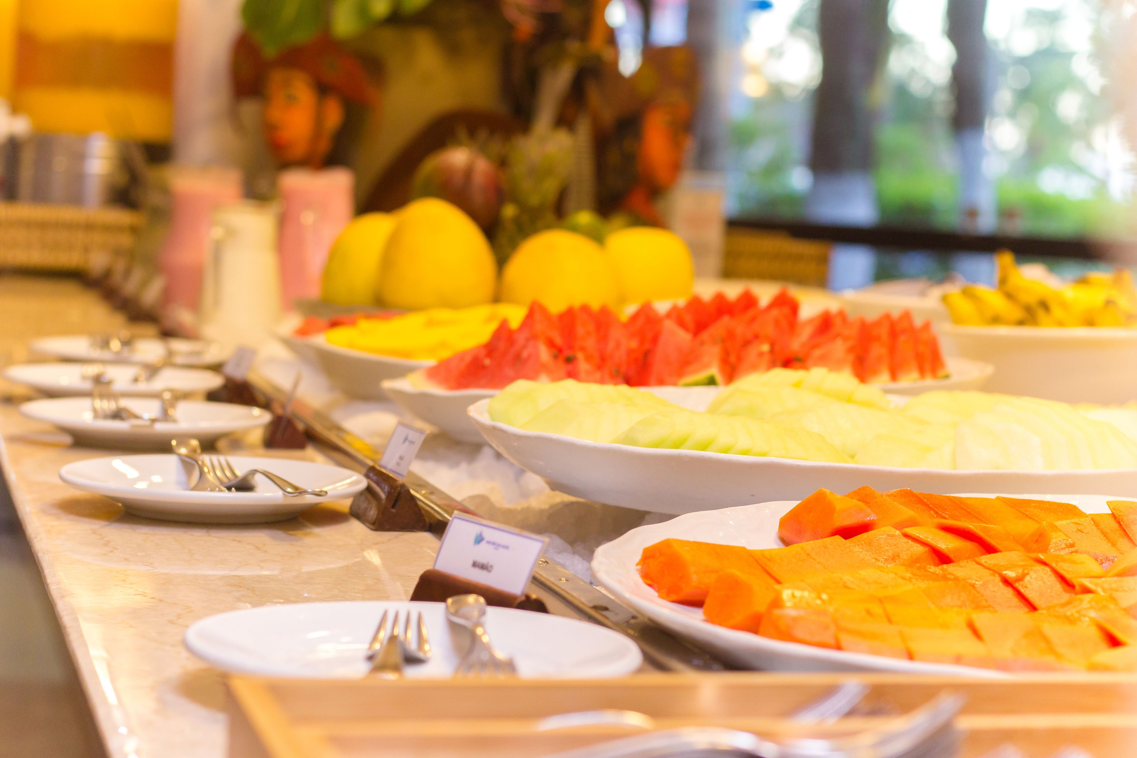 Un buffet proposant une variété de fruits et de légumes, notamment des pastèques et des mangues, disposés sur un comptoir avec des assiettes et des couverts.