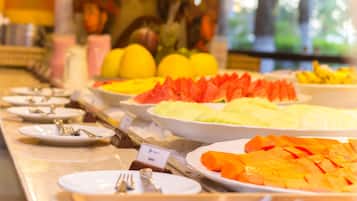 Un buffet proposant une variété de fruits et de légumes, notamment des pastèques et des mangues, disposés sur un comptoir avec des assiettes et des couverts.