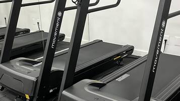 Three stationary treadmills in a room with a tiled floor and white walls.