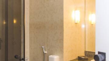 Un baño con mampara de vidrio, secador de manos y espejo con luces empotradas.