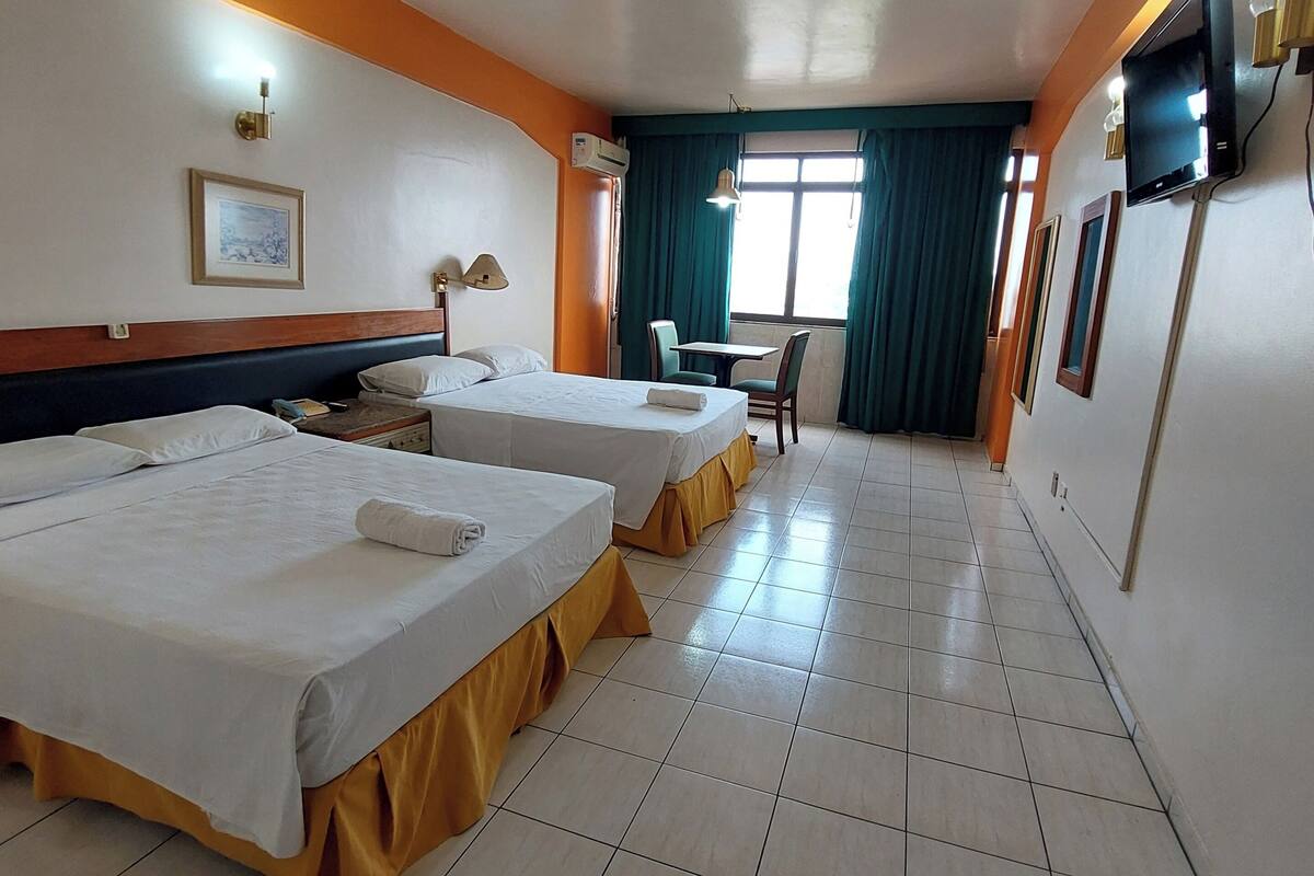 A hotel room with two beds, a desk, a chair, a TV, and a window with curtains.