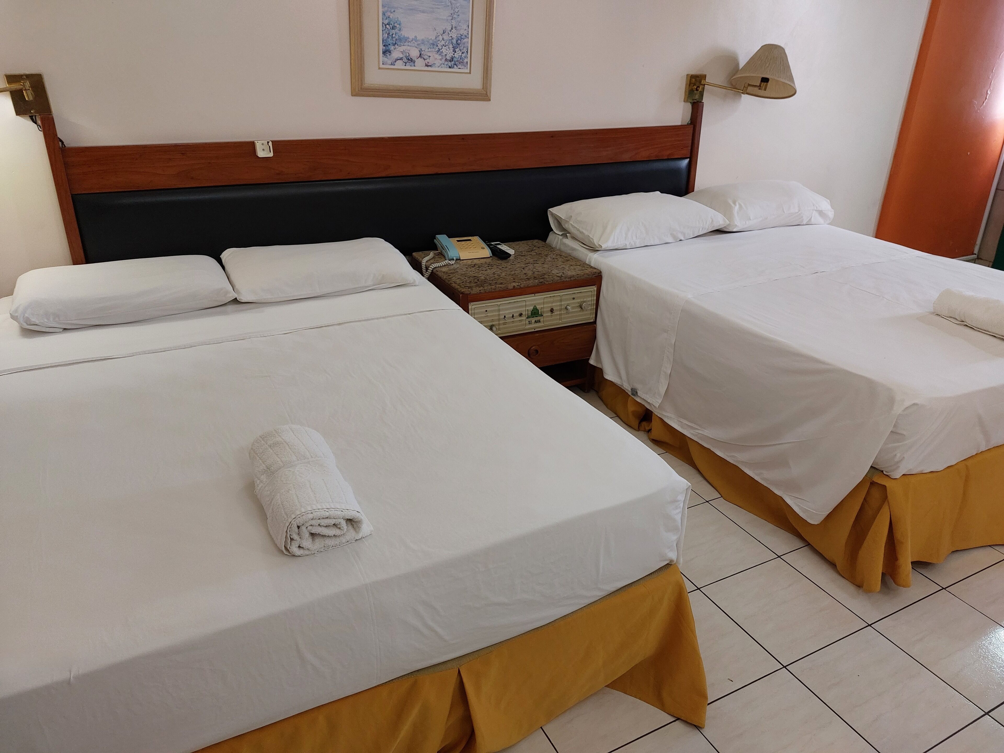 Une chambre d’hôtel avec deux lits, une table de chevet, une lampe et un tableau au mur.