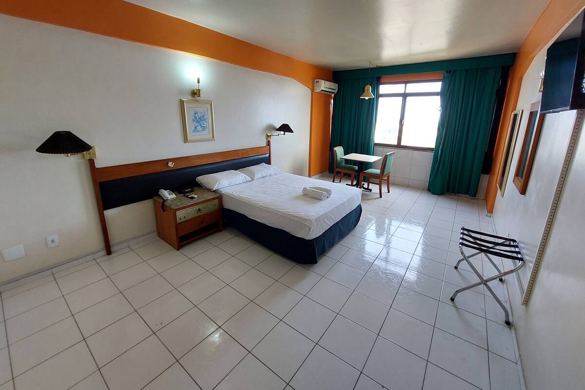 A hotel room with a bed, bedside table, lamp, air conditioning unit, and a small table with chairs.