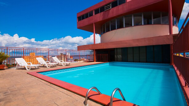 A swimming pool with lounge chairs and a red building with large windows. - GoldMen Business Manaus - Taj Mahal (Manaus)
