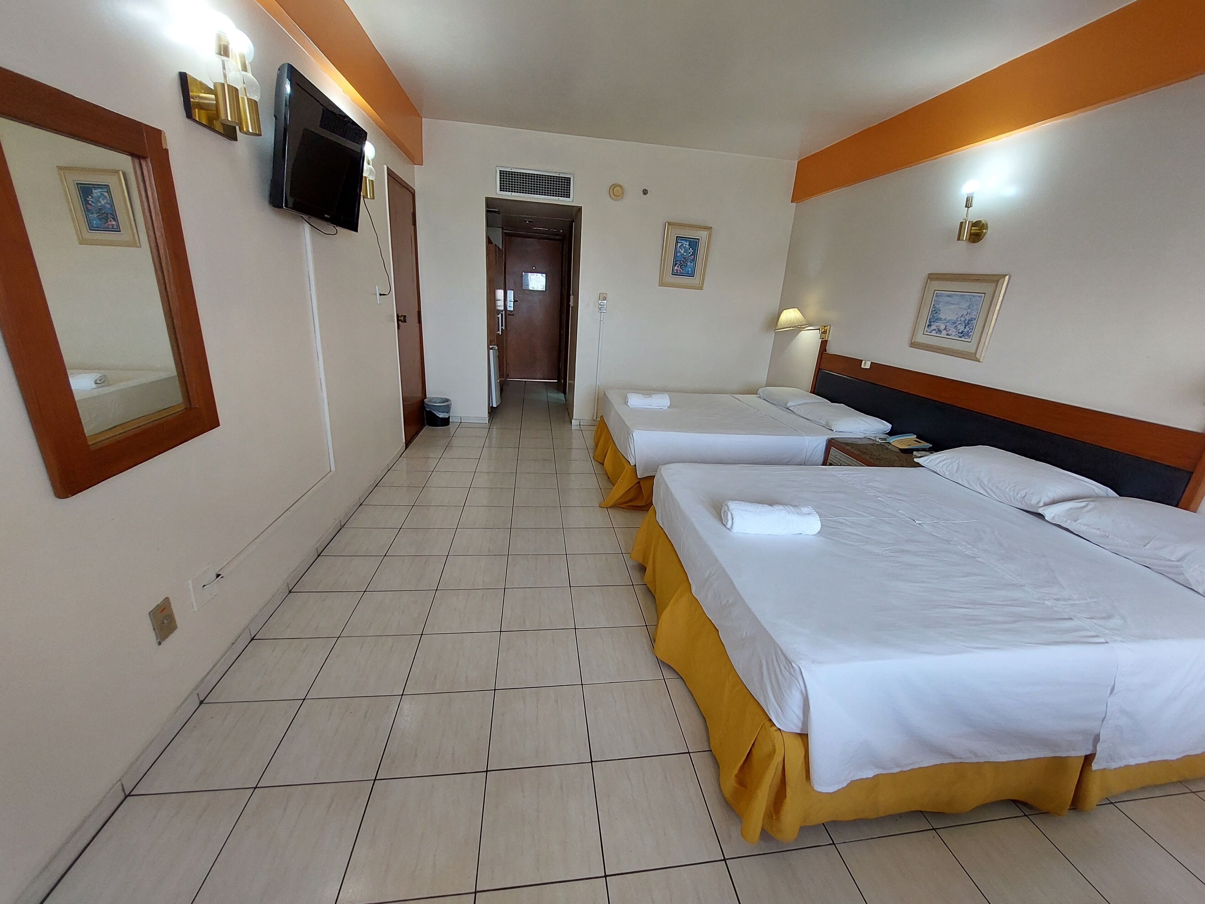 Una habitación de hotel con dos camas, un televisor y un pasillo que conduce a otra habitación.