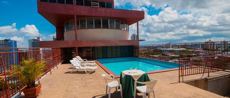 A rooftop pool area with a pool, lounge chairs, and a table with a green tablecloth.