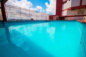 Una piscina con agua azul cristalina, una barandilla de metal y una vista del horizonte urbano al fondo.