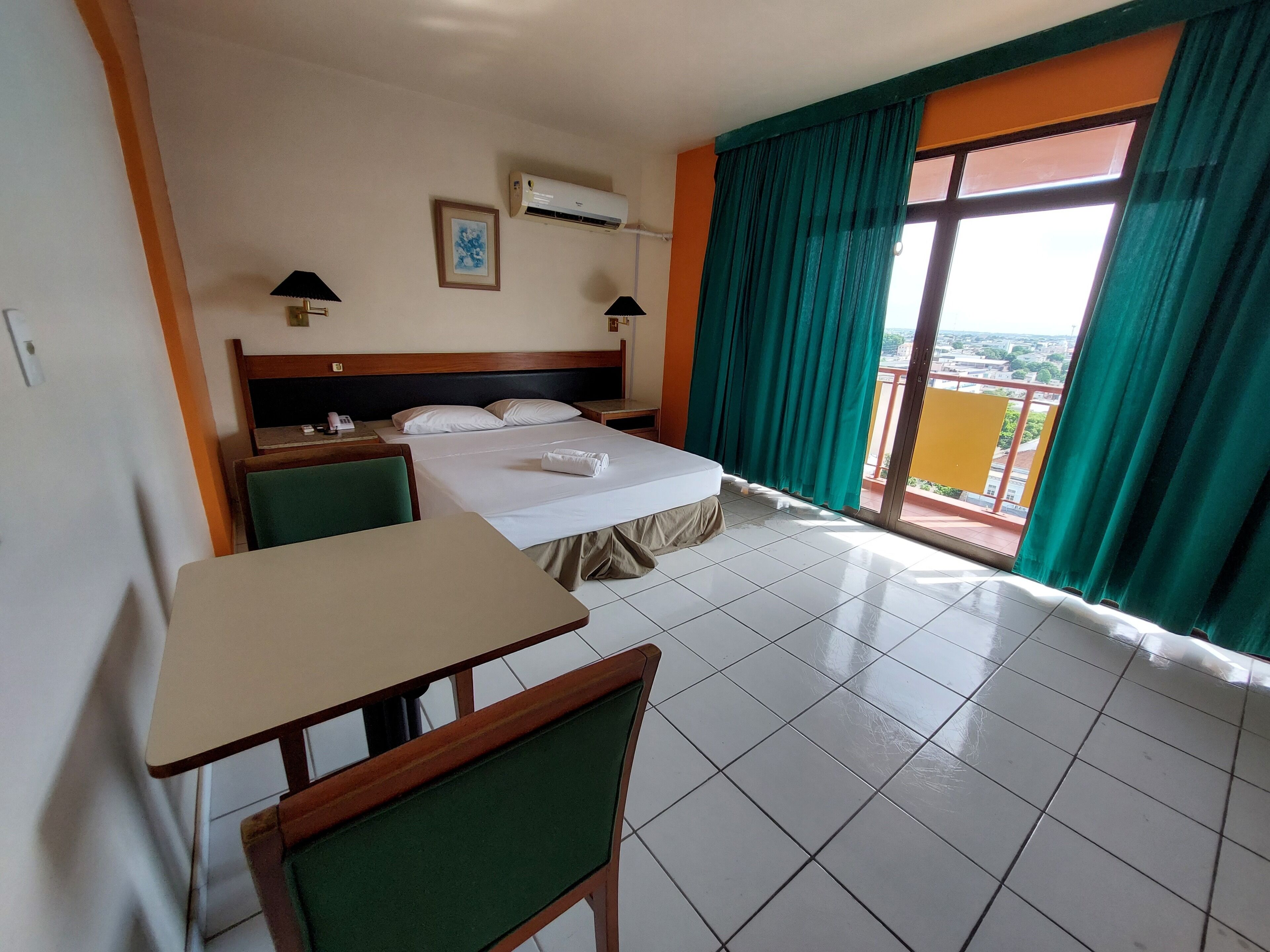 Ein Hotelzimmer mit Bett, Tisch, Stühlen, Klimaanlage, einem Bild an der Wand und Blick durch ein Fenster.