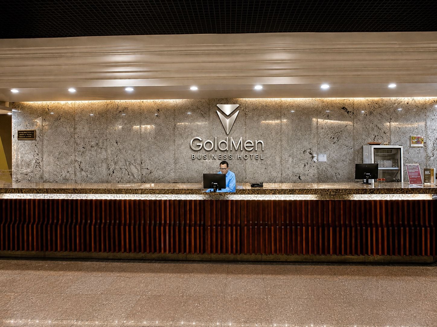 A reception desk at the GoldMen Business Hotel with a marble wall and a logo above.