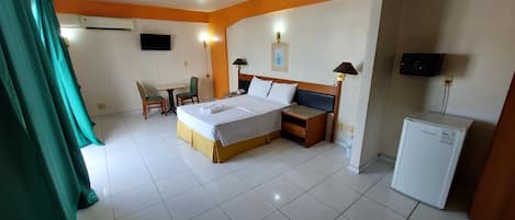 Habitación de hotel con cama, escritorio, silla, televisor, lámpara y refrigerador.