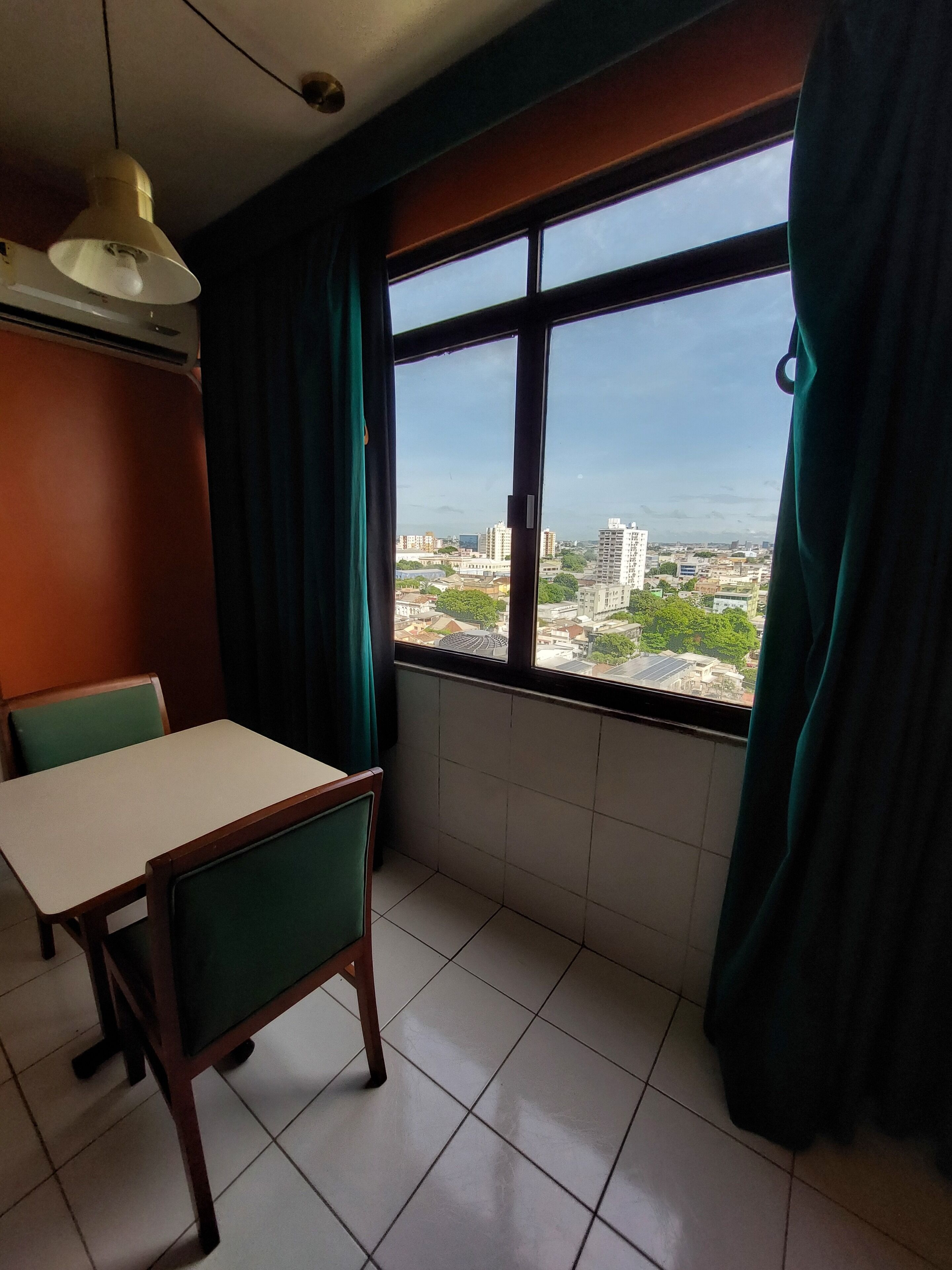 Una habitación con una mesa de comedor y sillas, una ventana con cortinas y vista a un paisaje urbano.