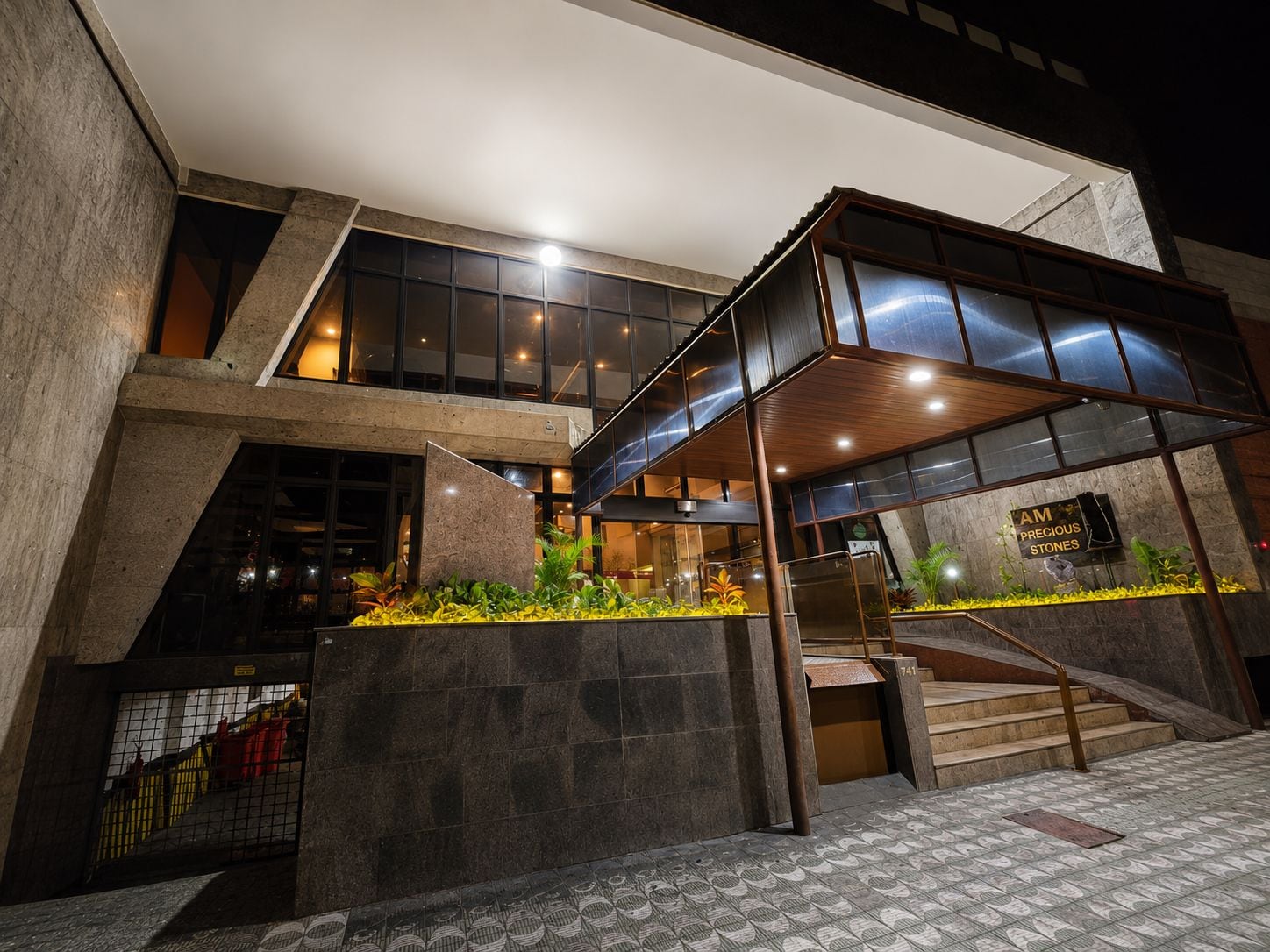 Un edificio moderno con fachada de vidrio, una escalera y un letrero que dice 'AM Precious Stones'.