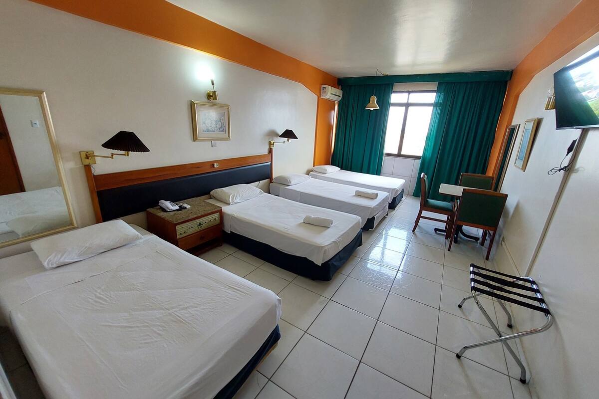 A hotel room with three single beds, a desk, a chair, and a TV.
