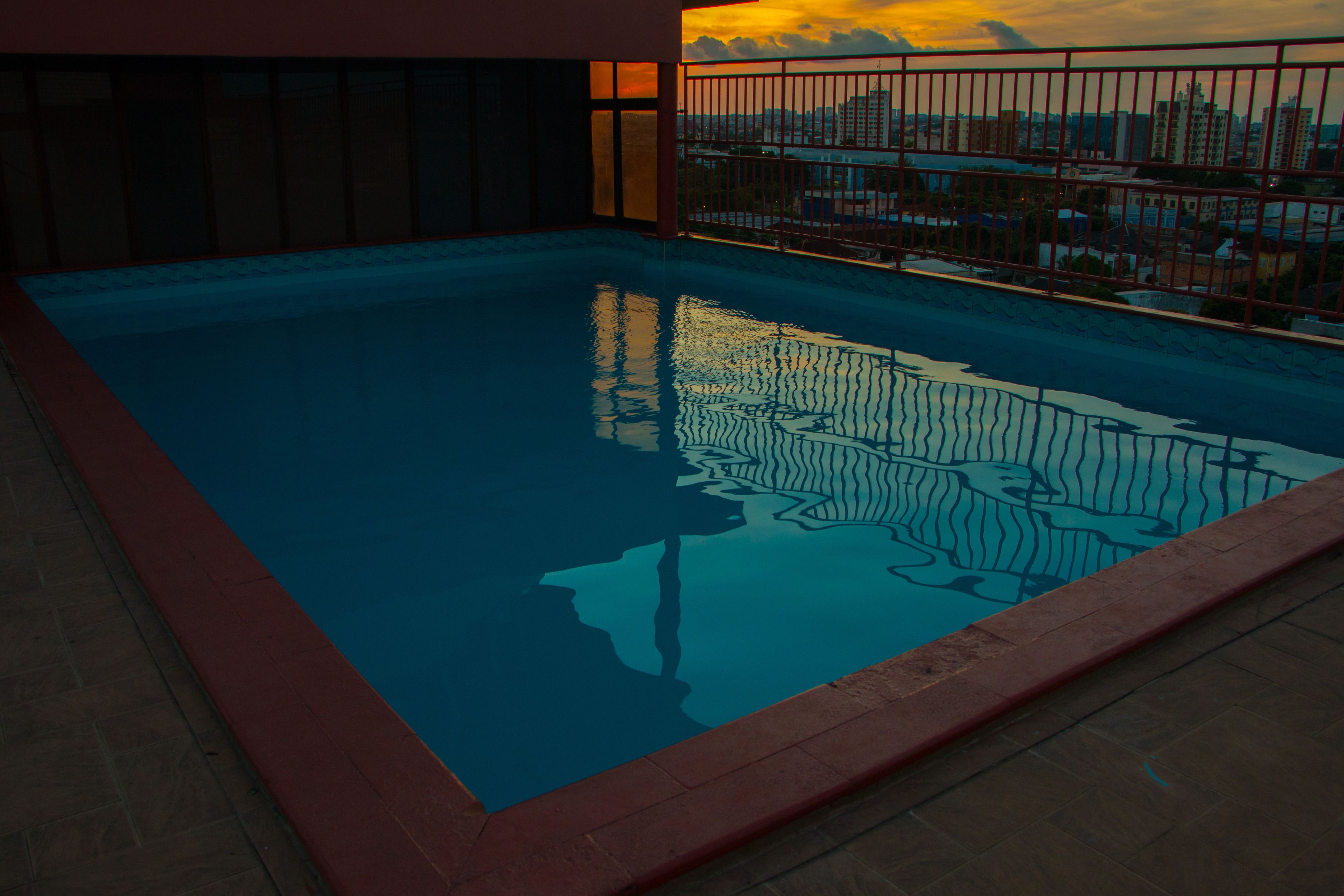 A swimming pool with a red border, surrounded by a metal fence, and a cityscape view in the background.