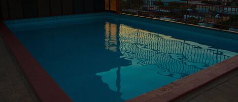 A swimming pool with a red border, surrounded by a metal fence, and a cityscape view in the background.