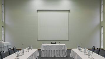 Un salón de conferencias con una larga mesa, sillas, botellas de agua y vasos.