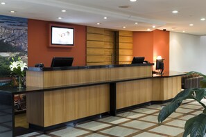 A reception desk with a wooden finish, a large screen above it, and a check-in counter. - Piazza Navona Porto Alegre by Intercity (Porto Alegre)