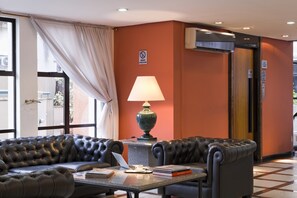 A hotel lobby with a leather sofa, a table with a laptop, books, and a lamp. - Piazza Navona Porto Alegre by Intercity (Porto Alegre)