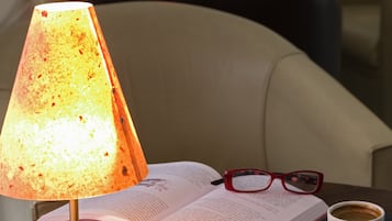 Een tafel met een lavalampe, een open boek, een paar brillen, een kop koffie en een schaaltje suikerklontjes.