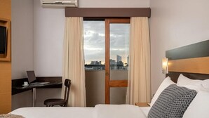 A hotel room with a bed, a desk with a laptop, a chair, and a view of the city through a glass door. - Piazza Navona Porto Alegre by Intercity (Porto Alegre)